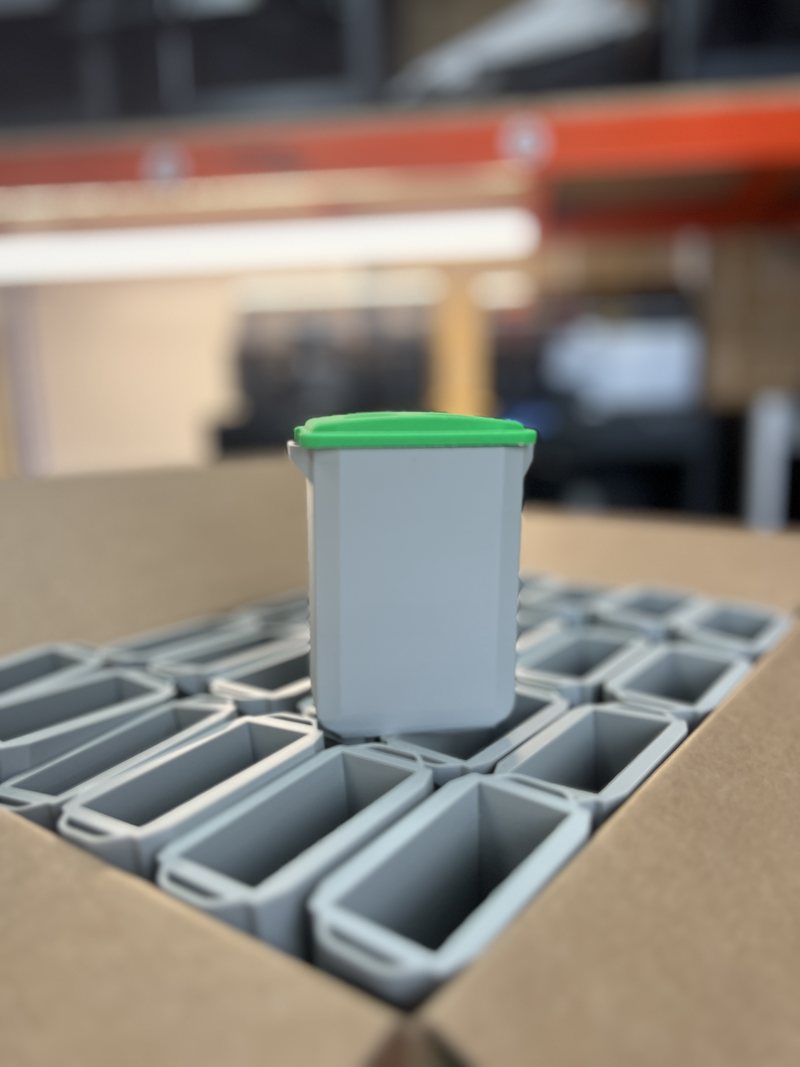 Batch of grey 3D-printed enclosures with green snap-fit lids, packed in a box ready for dispatch