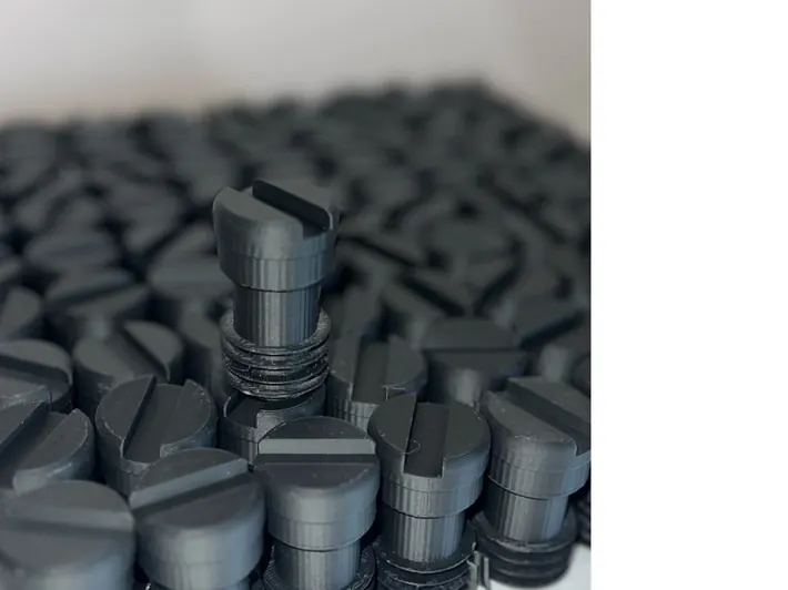 Macro photo of a 3DPE batch run · approximately fifty identical small black knobs printed and laid out for QC
